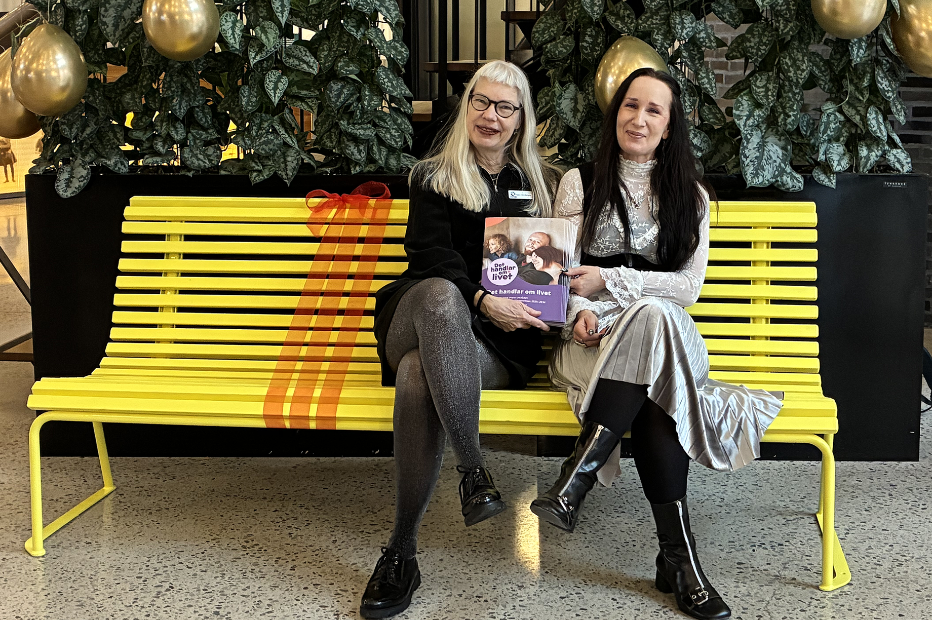 Två kvinnor sitter på en gul bänk