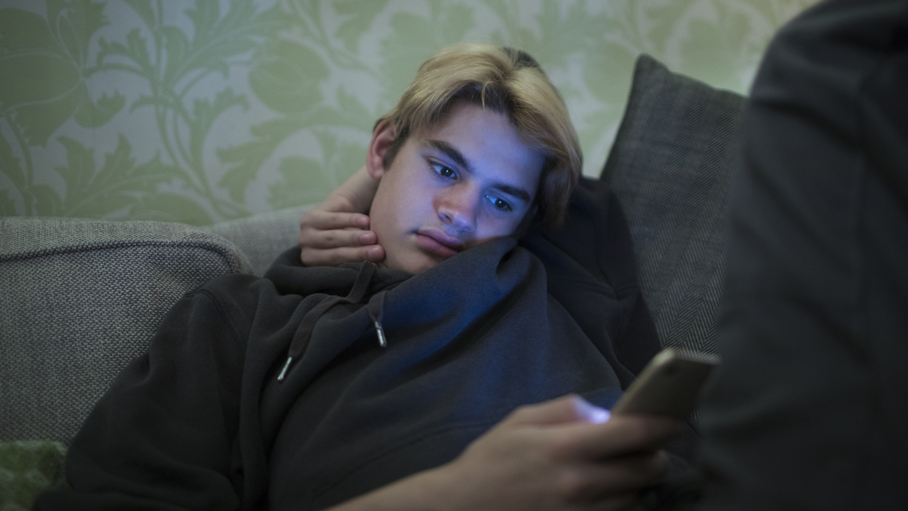 En ung kille sitter i soffa med en mobil i handen. Foto: Caia Image/John&eacute;r Bildbyr&aring;