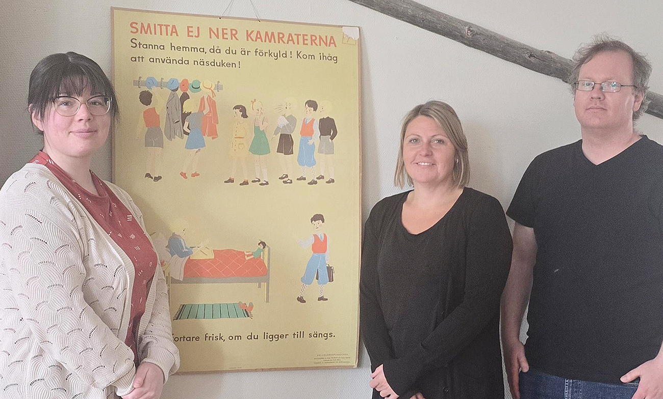Tre personal st&aring;r framf&ouml;r en gammal plansch