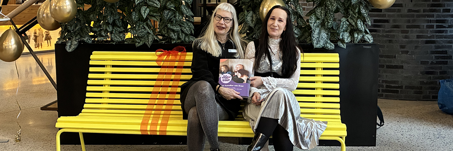 Två kvinnor sitter på en gul bänk