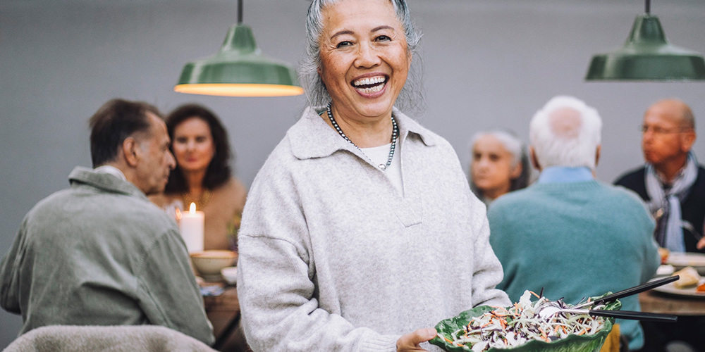 Äldre kvinna med asiatiskt ursprung håller en skål med sallad.