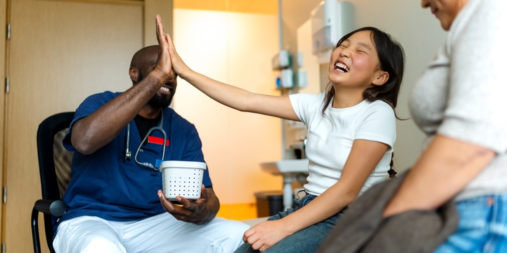 Ett barn gör high-five med vårdpersonal. Mamma sitter bredvid.