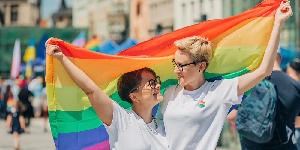 Två personer som tittar på varandra och håller i en Prideflagga.